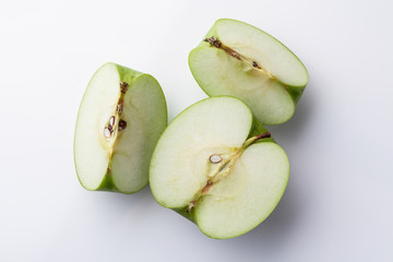 Sliced green apple half and two quarters on white background directly from above