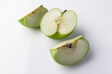 Sliced green apple half and two quarters on black background from high angle