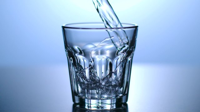 Wasser wird in Glas gesch&uuml;ttet, Zeitlupe, blauer Hintergrund
