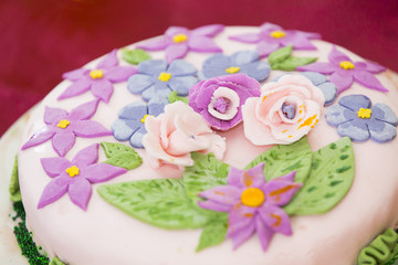 Obraz na płótnie Canvas Праздничный торт в пастельный тонах, украшенный нежно-розовой кондитерской мастикой и кремовыми цветами фиолетового, голубого, розового и зеленого цветов 