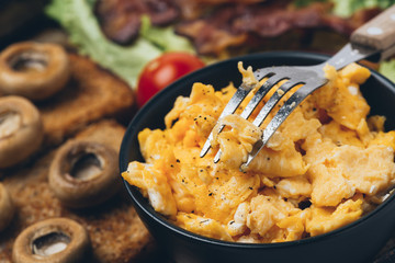 Close shot of tasty and fresh traditional meal with toast, scrambled eggs, fried bacon, mushrooms, green salad and cherry tomatoes.
