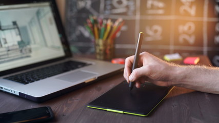 Creative businessman writing on graphic tablet while using laptop in office