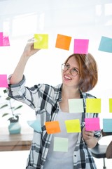 smiling hipster woman sticking notes on a notice board