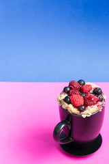 Mug Cake with Berries Prepared in Microwave on Pink and Blue Funny Background, Vertical View, Free Space for Text