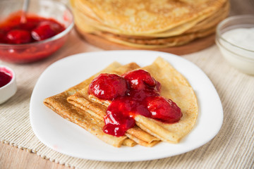 Thin Russian pancakes folded triangle with strawberry sauce on a white plate, close-up, side view