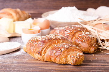 Ingredients for baking croissants - paper, flour, wooden spoon, rolling pin, eggs, egg yolks, butter served on a rustic wooden tray table.