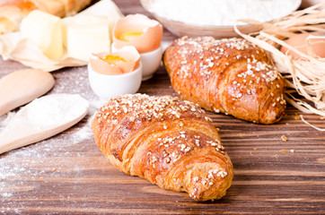 Ingredients for baking croissants - paper, flour, wooden spoon, rolling pin, eggs, egg yolks, butter served on a rustic wooden tray table.