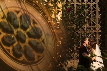 Lovely groom and bride kissing and holding outside, with a churc