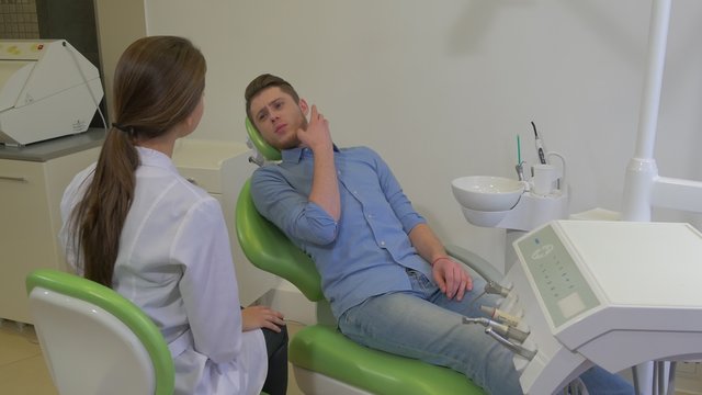 Dentist is Listening to a Patient's Complaints Client is Gesticulating Anxious Man is Talking Room of Dental Clinic Young Female Doctor Male Client