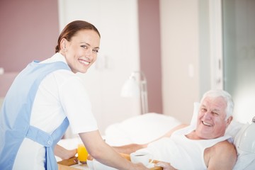 Obraz na płótnie Canvas Portrait of nurse offering breakfast to senior man lying on bed