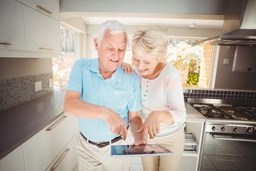 Happy senior couple holding digital tablet in kitchen