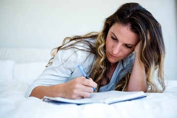 woman lying in her bed writing in a book