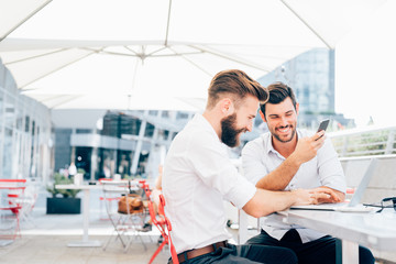Two young contemporary businessmen working outdoor sitting in a
