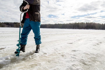 Fototapeta na wymiar ice fisherman drills using a bore on the lake in winter on a sunny day in the woods