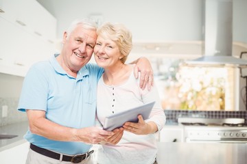 Portrait of happy senior couple holding tablet in kitchen