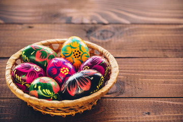 Beautiful painted colorful Easter eggs in a wickerwork basket on old brown wooden background