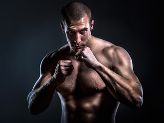 fighter posing shirtless and with bare knuckles in guard stance on dark background