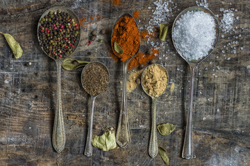 Spoons filled with colorful spices on rustic wooden table - closeup
