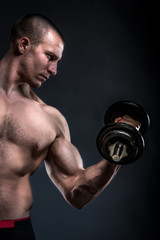 Fototapeta na wymiar bodybuilder lifting dumbbells on dark background with copy space