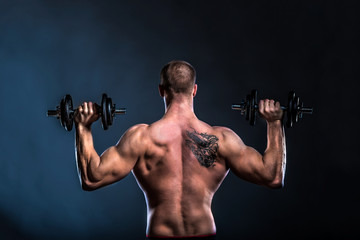 Fototapeta na wymiar strong man bodybuilder lifting dumbbells on dark background back view