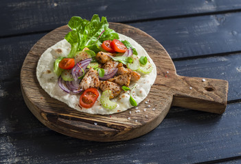 Delicious grilled chicken and fresh vegetables homemade tortilla on a rustic cutting board on a dark wooden background