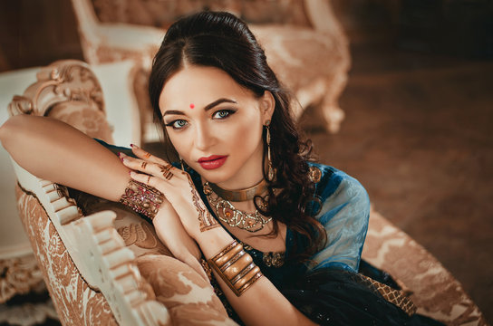 portrait of a beautiful woman in Indian traditional Chinese dress, with her hands painted with henna mehendi. Girl sitting on a luxury sofa