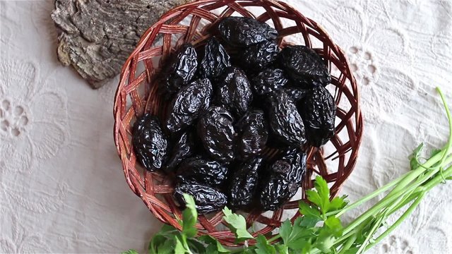Group of prunes (dried plums) on a white tablecloth with parsley and decoration. Shot from above, rotating