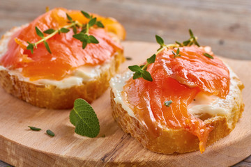delicious sandwich with smoked salmon, cream cheese and thyme on wooden board