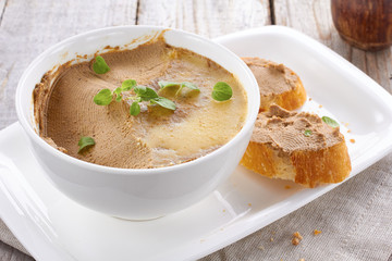 Homemade chicken liver pate on baquette and in white bowl