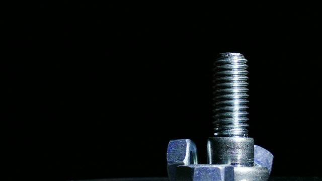 One bolt and three nuts rotates against  dark background. 4K shot