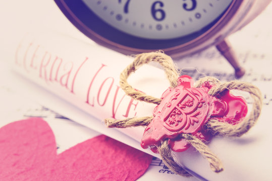 Rolled up scroll of love poem fastened with natural brown jute twine hemp rope, sealed with sealing wax and stamped with alphabet letter B. Decorated with a red mulberry paper heart and vintage clock.