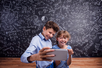 Boy and girl  with smartphone, taking selfie, against blackboard