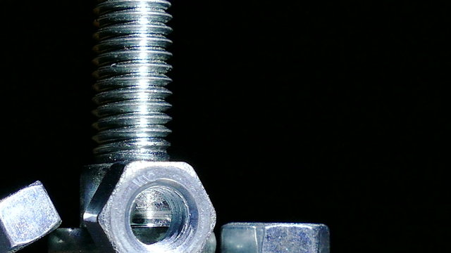 Bolt and three nuts rotates against  dark background. 4K  close up left side