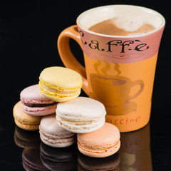 High cup of cappuccino coffee and macaroon on a black background