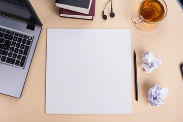 Office table desk with set of colorful supplies, white blank note pad, cup, pen, pc, crumpled paper, flower on beige background. Top view and copy space for text