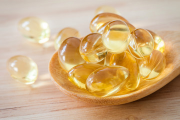 Fish oil supplement capsule on wooden spoon and wooden backgroun