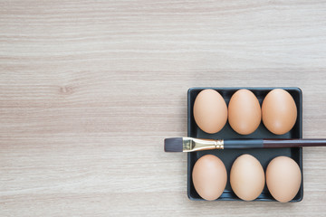 Six eggs in black square plate with a brush on wooden surface with space for text