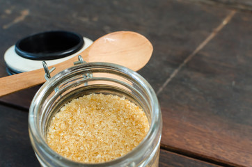 brown sugar with wooden spoon in bottle on wood table, selective focus.