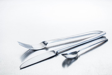 Glänzende Gabel, Teelöffel und Messer aus Edelstahl angeordnet auf einer Edelstahlplatte