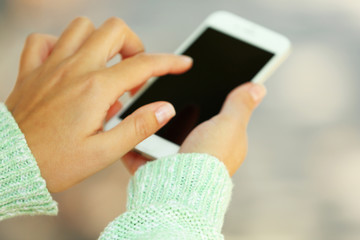 Female hands holding a mobile phone outdoors, on blurred background