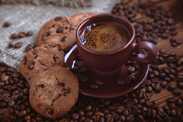 Roasted coffee beans, biscuit with chocolate and cup on the wooden background