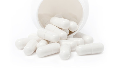 white medicine capsules pouring from bottle isolated on white ba