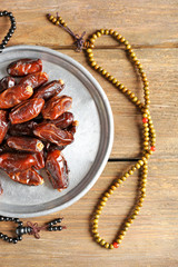 Composition of dried dates in holiday dish and rosary on wooden background