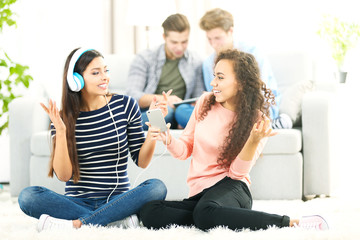 Two teenager girls listening to music with headphones in living room