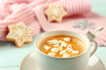 Cup of hot cacao with marshmallow, cookies and warm scarf on blue table