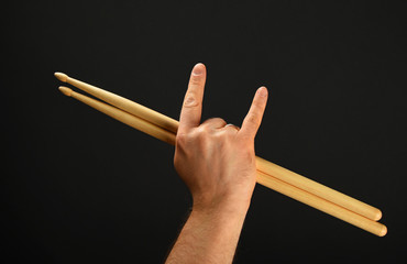Man hand with drumsticks and devil horns over black
