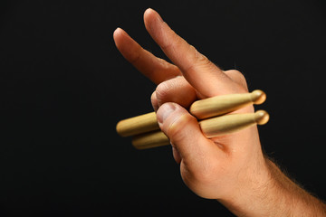 Man hand with drumsticks and devil horns over black