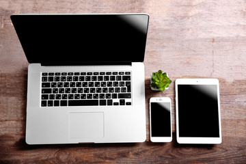 Modern laptop, smart phone and tablet with small green plant on a wooden table