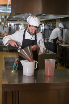 cook prepares a pureed strawberries through a strainer