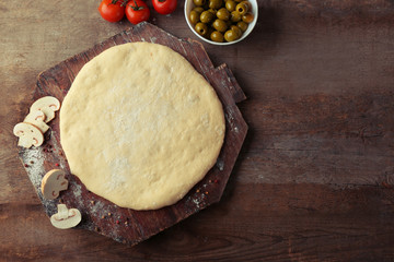 Fresh dough prepared for pizza with tomatoes and sliced mushrooms on a wooden board, close up